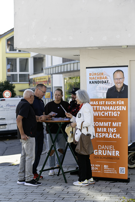 Begegnungen mit Daniel Gruner am 26. September Daniel Gruner steht gemeinsam mit vier Besuchern am Informationsstand vor seinem Wahlkampfaufsteller.