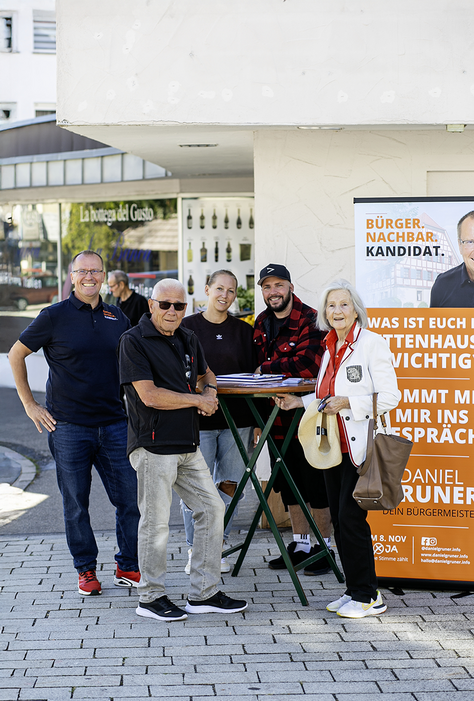 Bürgergespräche mit Daniel Gruner in Dettenhausen Daniel Gruner und mehrere Besucher unterhalten sich an einem Stehtisch neben einem Wahlkampfaufsteller.